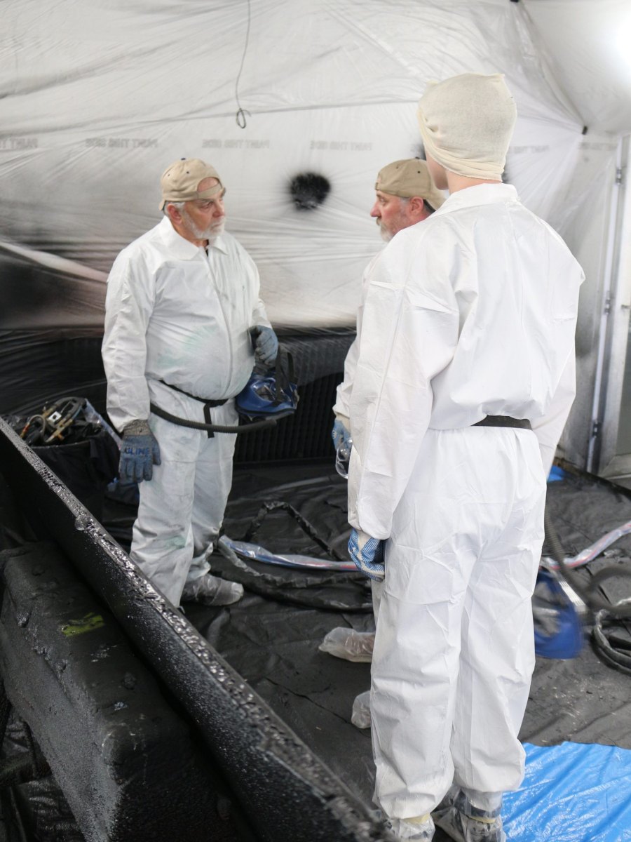 Two trainees standing over a freshly sprayed panel inside the booth
