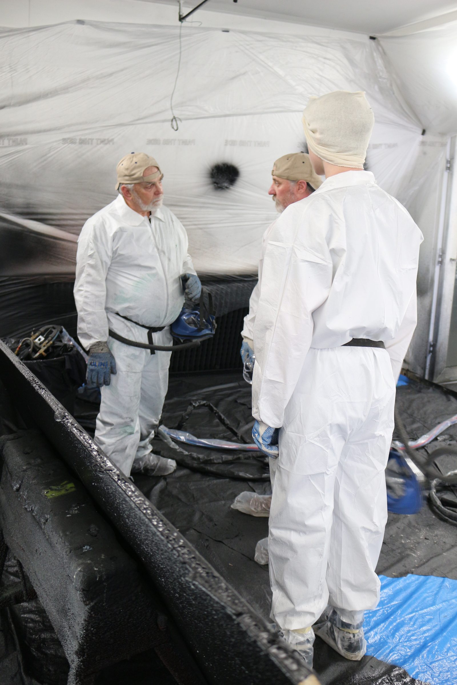 Two trainees standing over a freshly sprayed panel inside the booth
