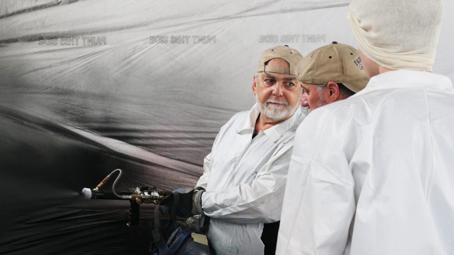 Instructor holding a heated spray gun and whip hose, turning to coach a trainee