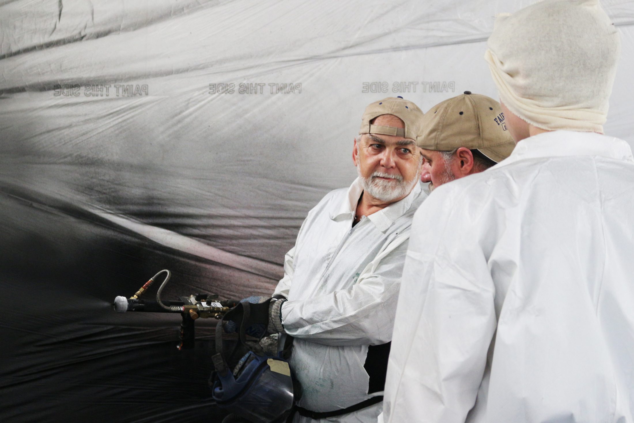 Instructor holding a heated spray gun and whip hose, turning to coach a trainee