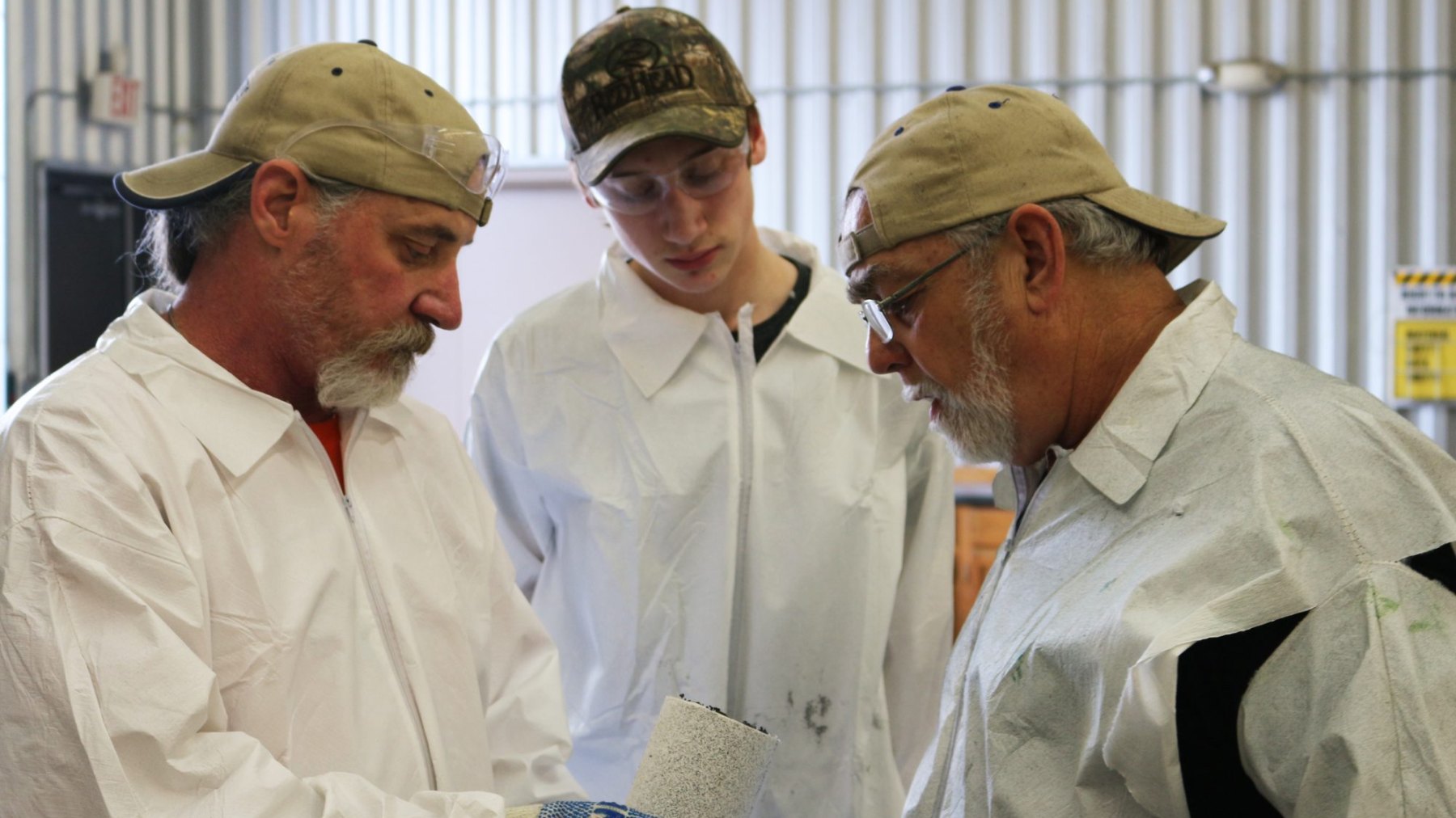 Two instructors and a young trainee examining a coated sample together