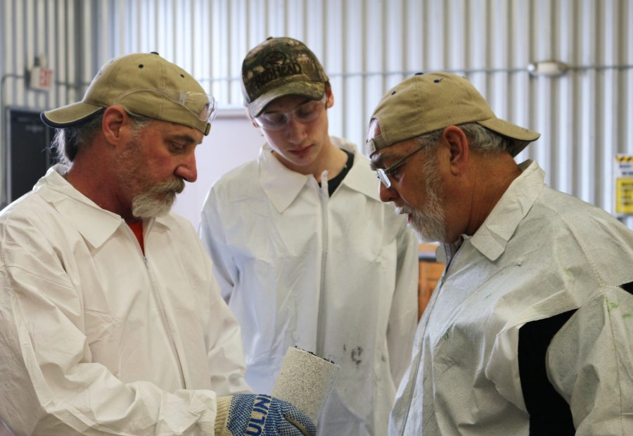 Two instructors and a young trainee examining a coated sample together