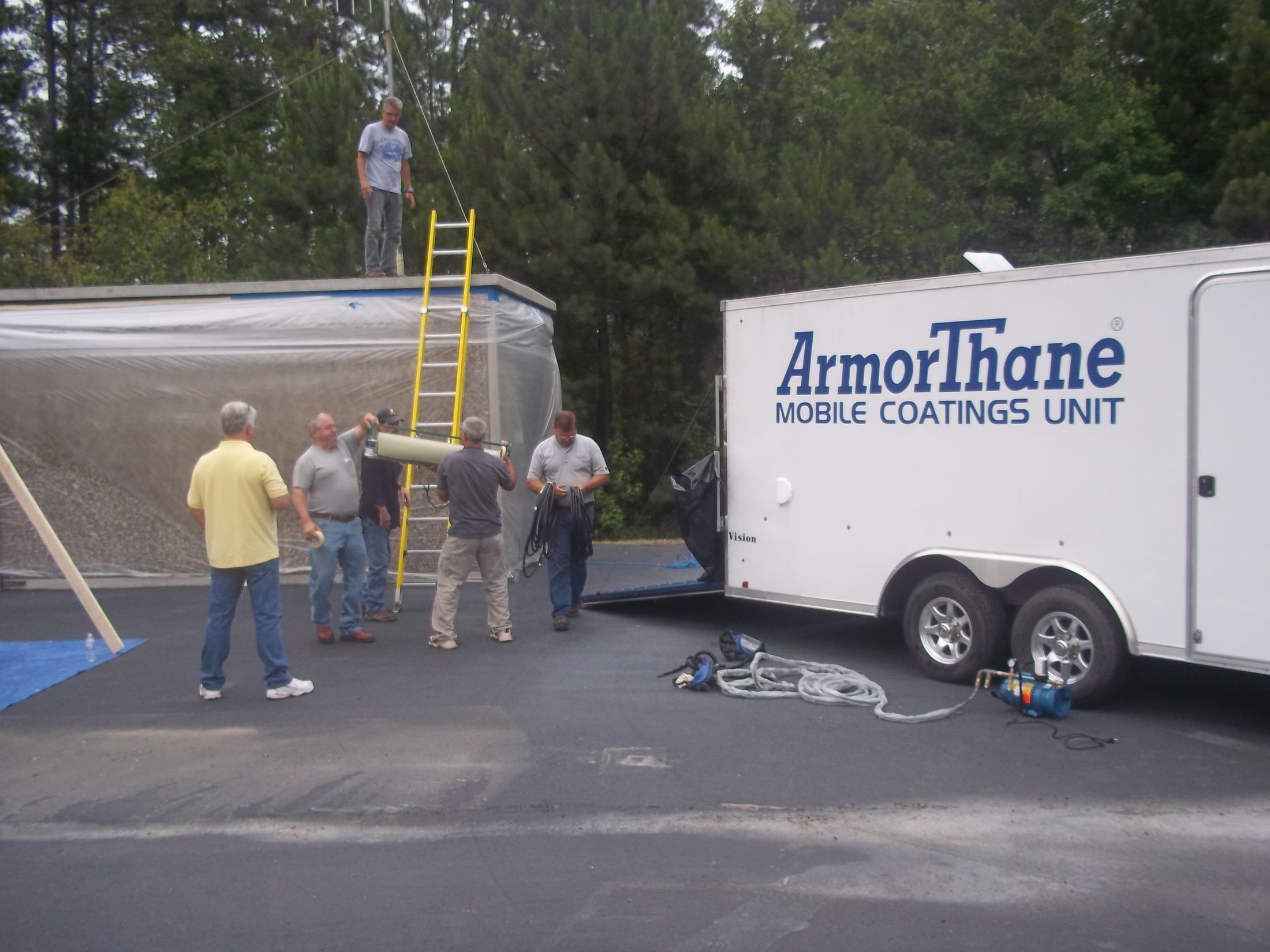 A class gathered around a temporary spray enclosure beside the ArmorThane Mobile Coatings Unit