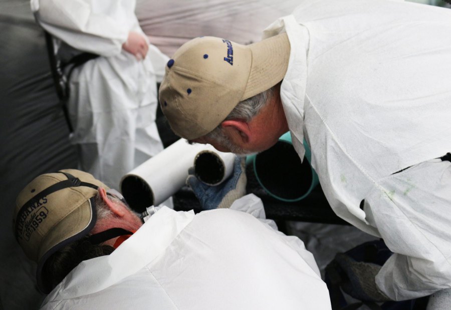 Instructor and trainee in respirators working over pipe sections on a bench