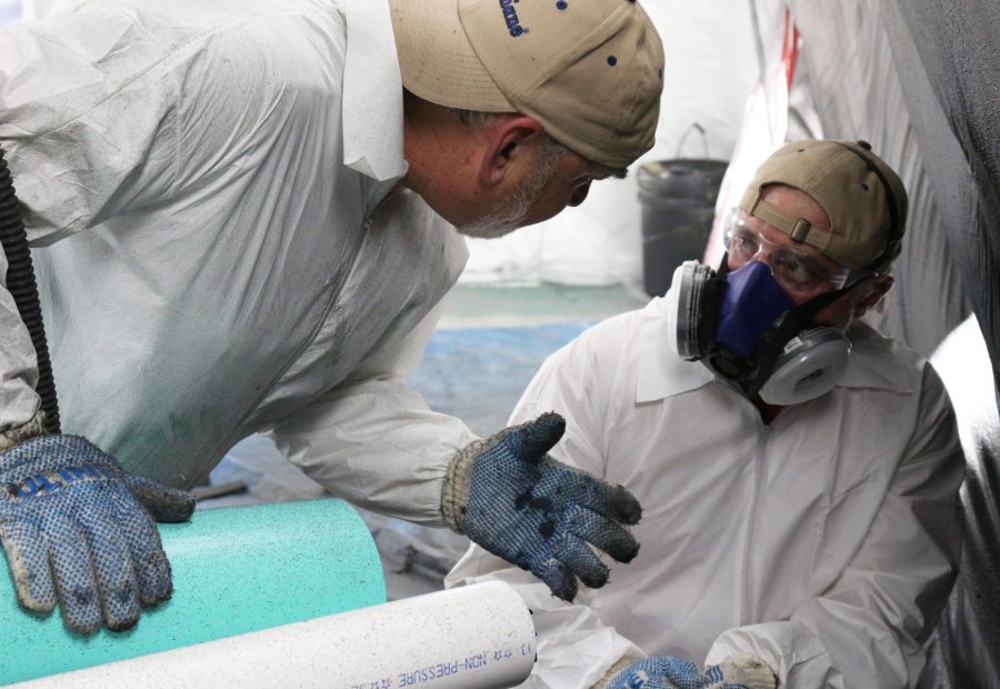 Gloved hands holding a pipe section while an applicator in a respirator works on it