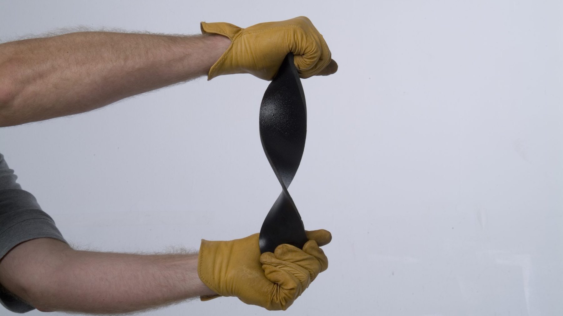 Two gloved hands stretching and twisting a cured polyurea sample to show its elongation