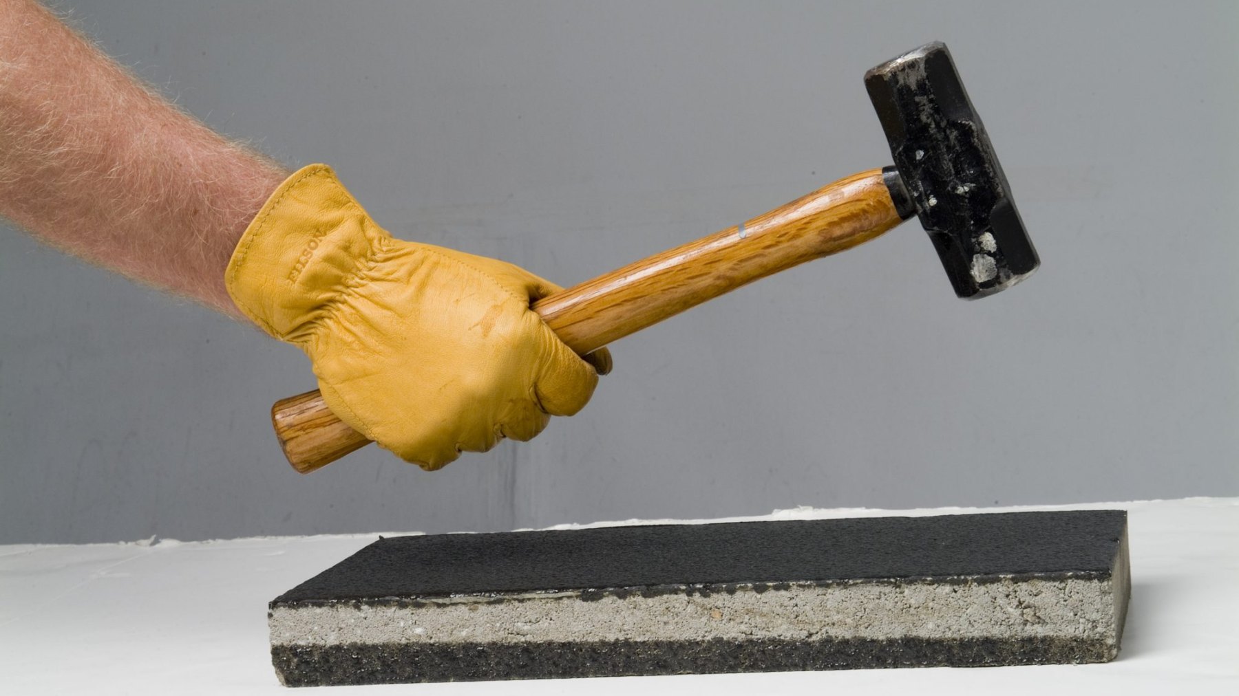 A gloved hand swinging a sledgehammer onto a polyurea-coated concrete block
