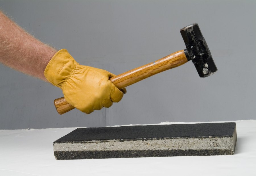 A gloved hand swinging a sledgehammer onto a polyurea-coated concrete block