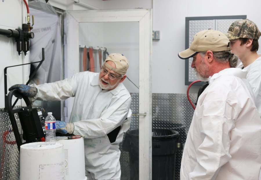 Instructor demonstrating a plural-component proportioner to two trainees