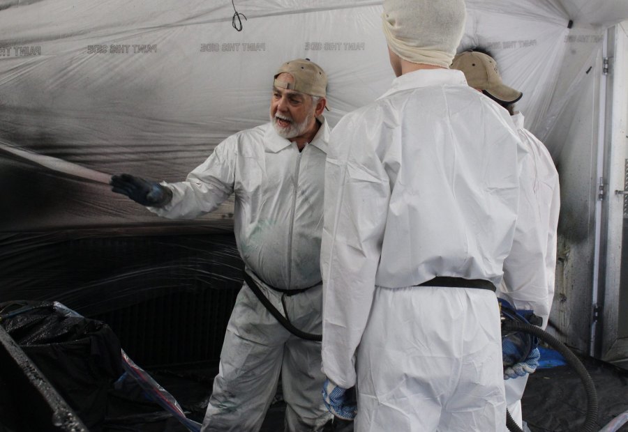 A trainee pulls the trigger on a plural-component spray gun with the instructor standing alongside