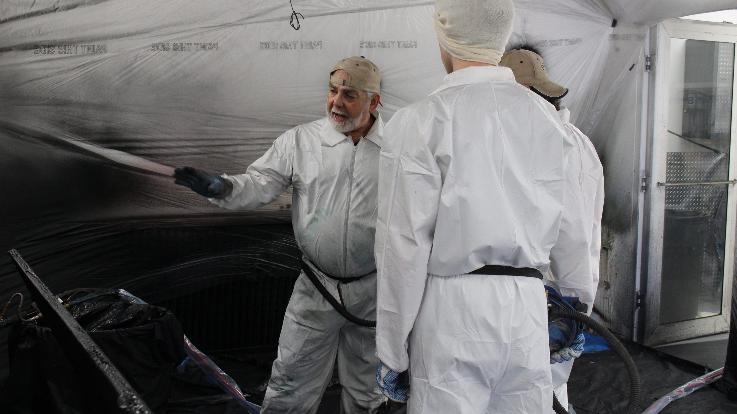 A trainee pulls the trigger on a plural-component spray gun with the instructor standing alongside